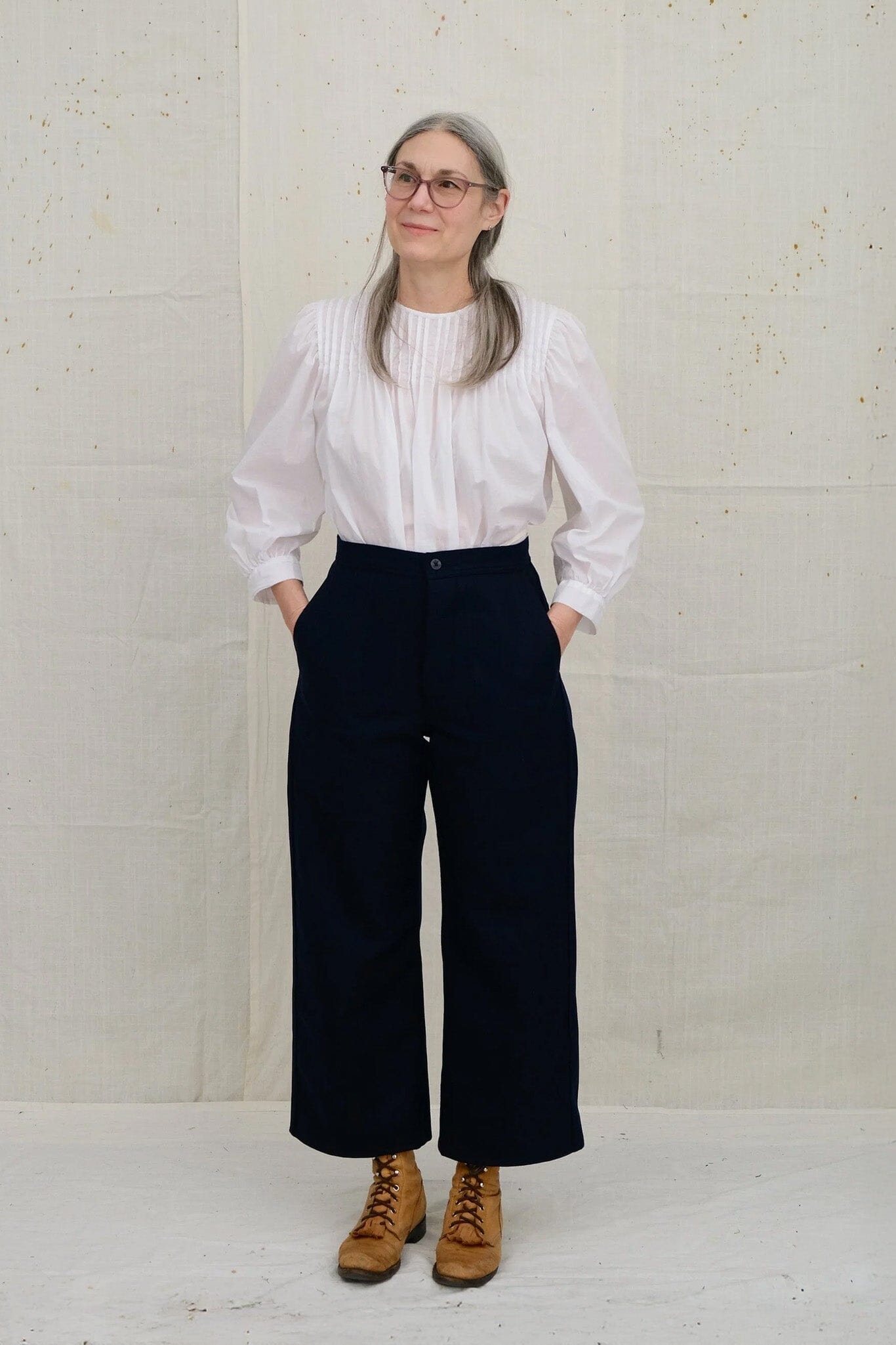 Person wearing a white blouse and dark navy pants against a plain background