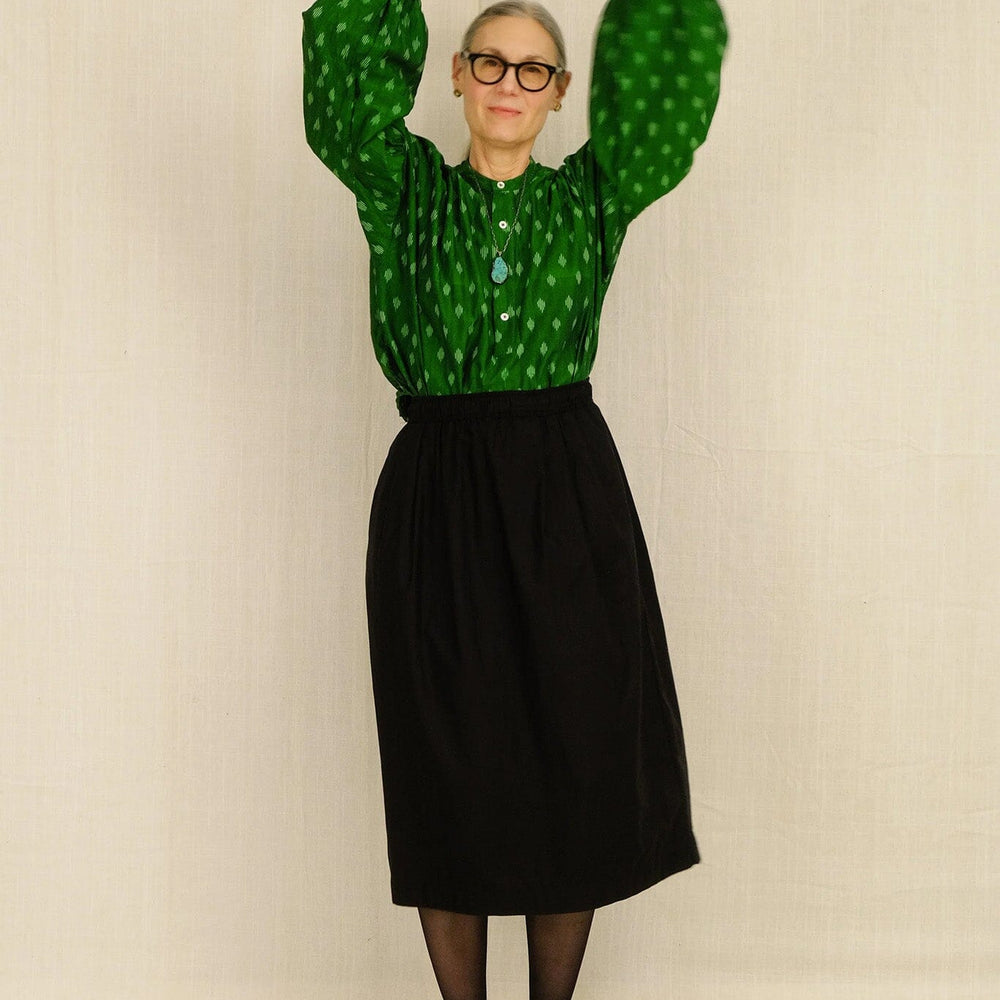 Woman wearing a green patterned blouse and black skirt against a plain background