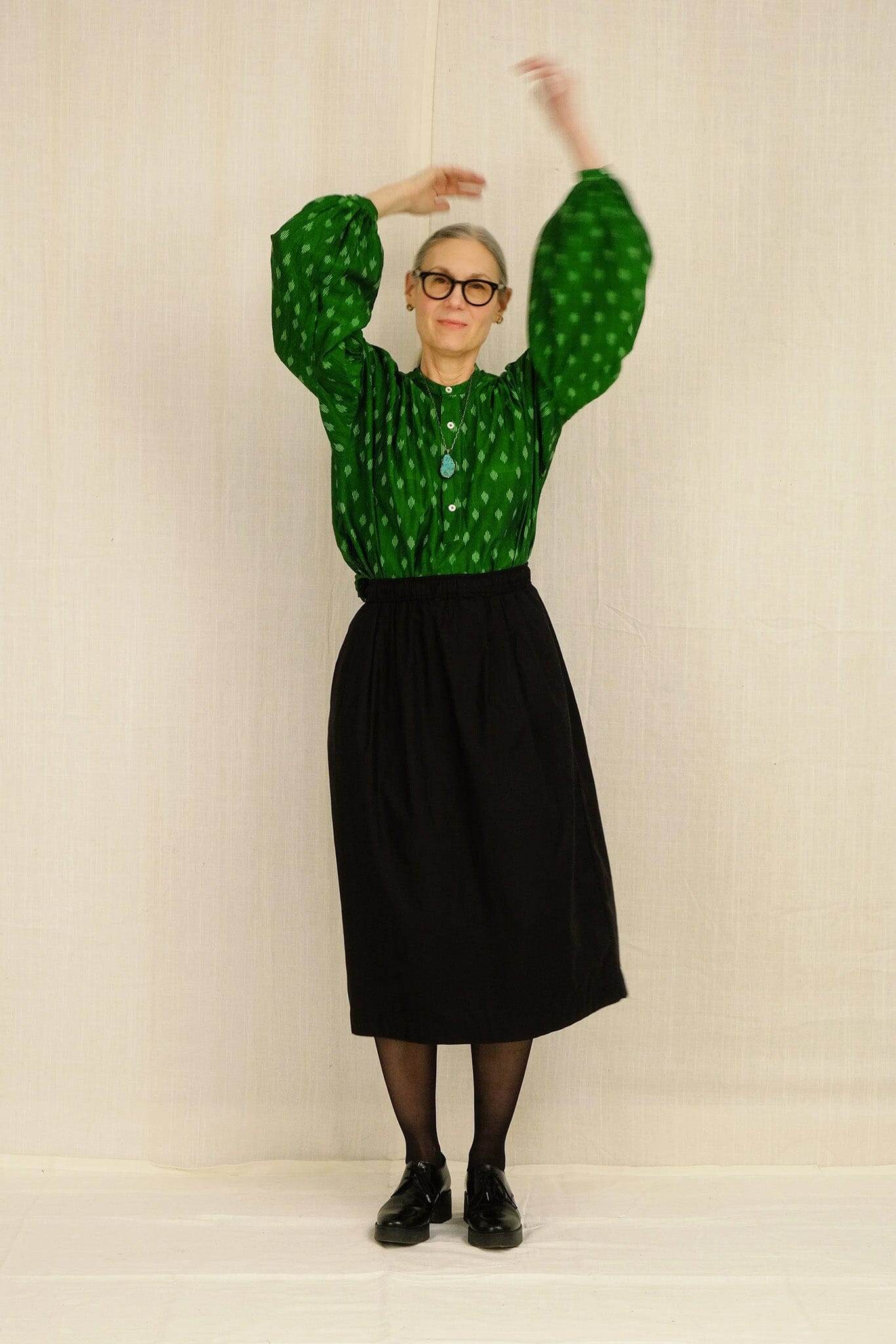 Woman wearing a green patterned blouse and black skirt against a plain background