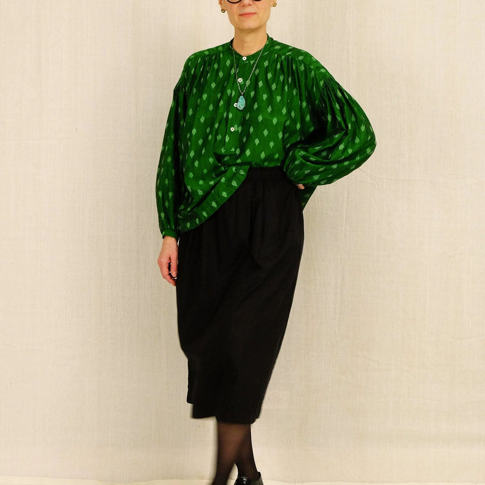 Woman wearing a green patterned blouse and black skirt against a plain background