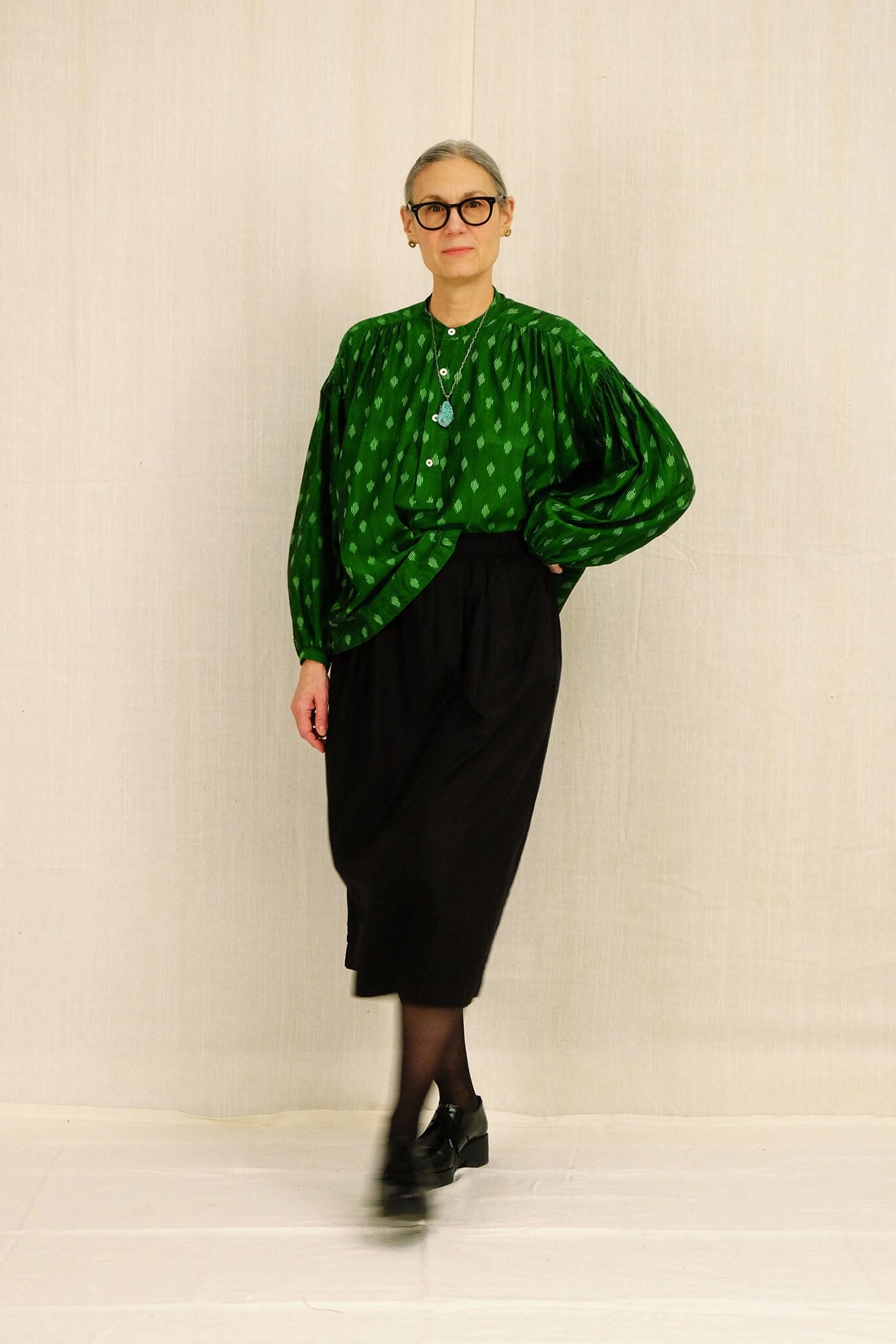 Woman wearing a green patterned blouse and black skirt against a plain background