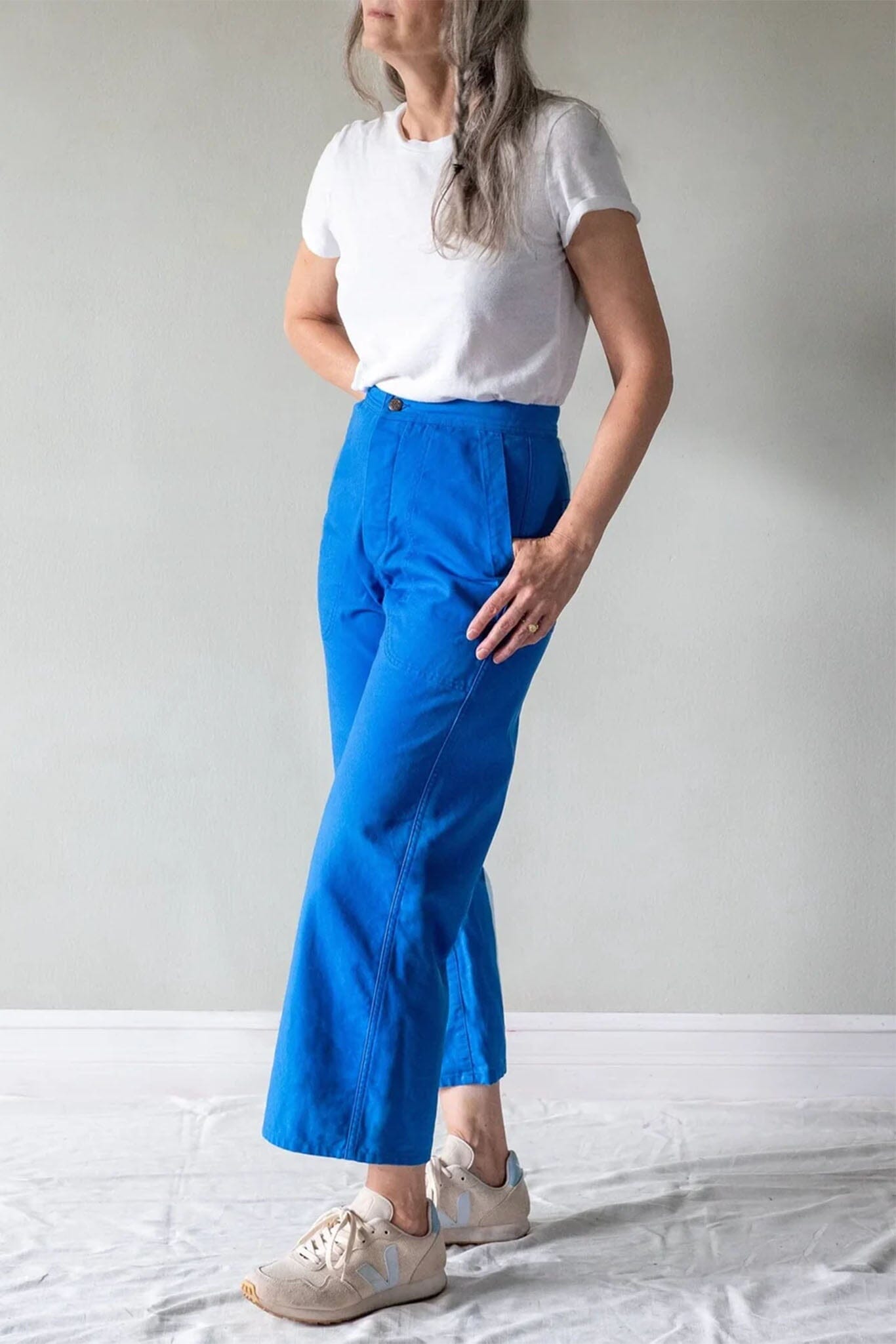 Person wearing a white t-shirt and blue pants standing against a plain background