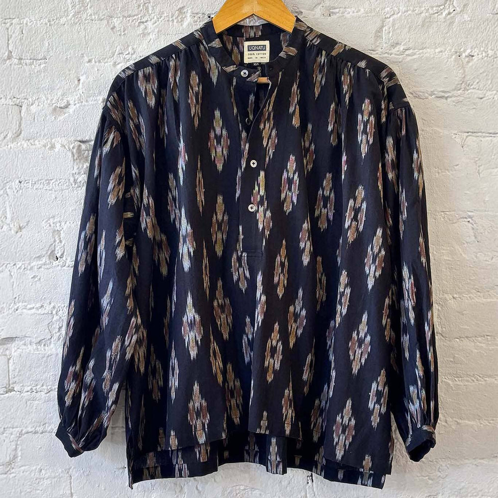 Patterned long sleeve blouse on a hanger against a white brick wall