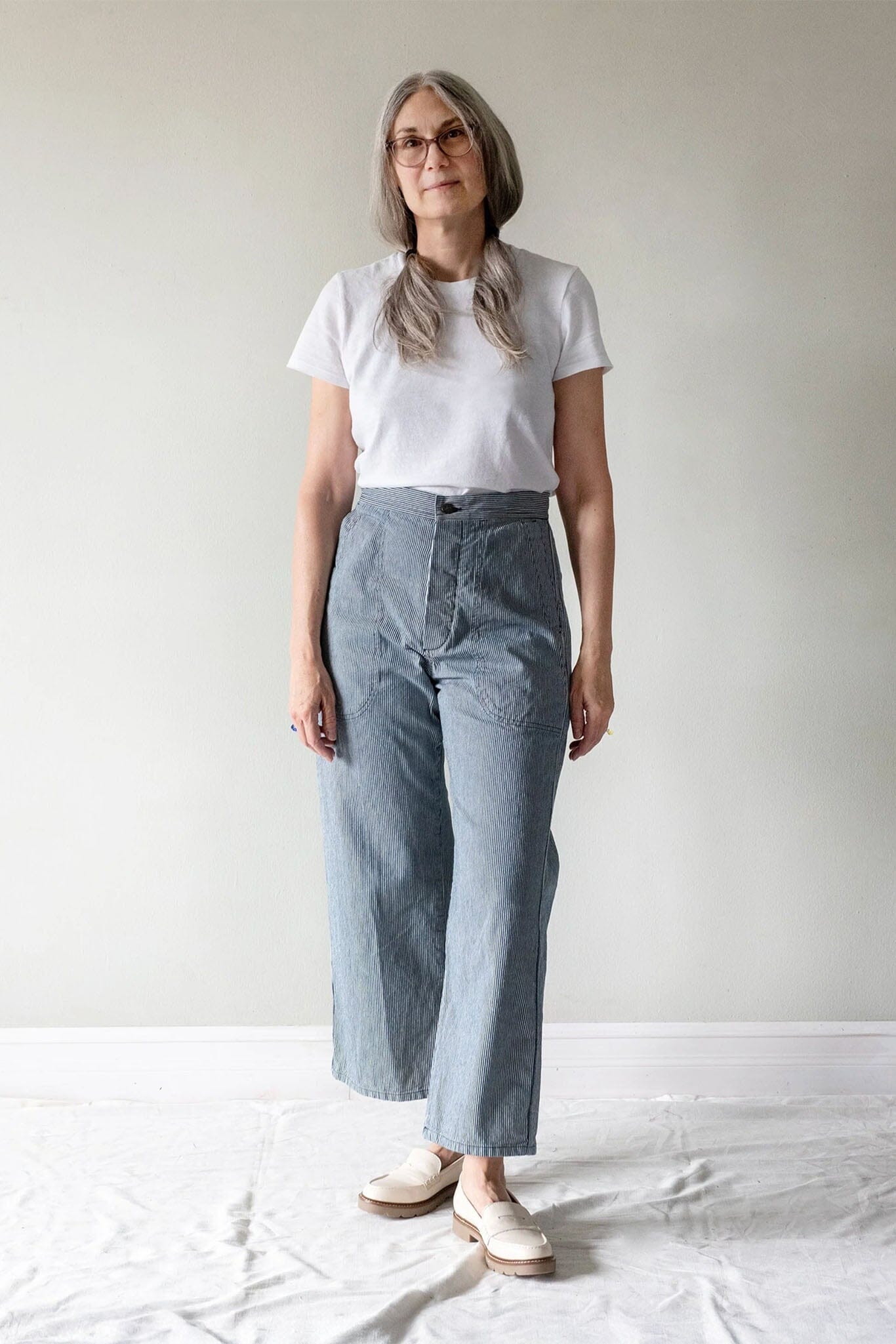 A woman wearing a white short-sleeve t-shirt and light blue wide-leg cropped pants, standing against a plain light gray wall.