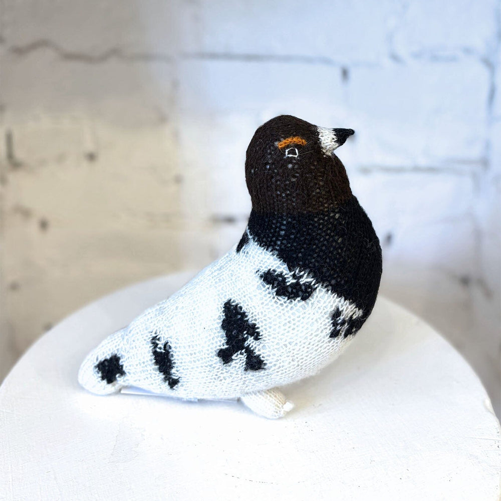 Knitted bird toy on a white surface with a light gray background