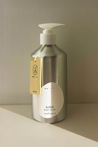 Silver bottle of 'AIRA' body lotion with a white pump on a beige surface and background.