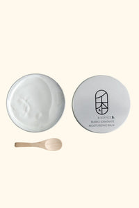 A container of moisturizing balm with a wooden spoon on a beige background
