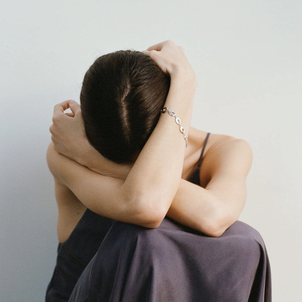 
                  
                    Person sitting with head in hands with silver bracelet against a plain wall
                  
                