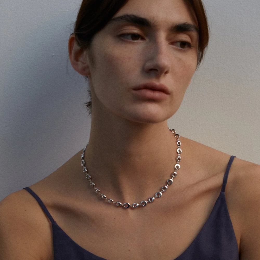 
                  
                    Woman wearing a silver circular necklace against a plain background
                  
                