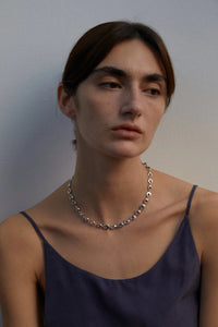 Woman wearing a silver circular necklace against a plain background