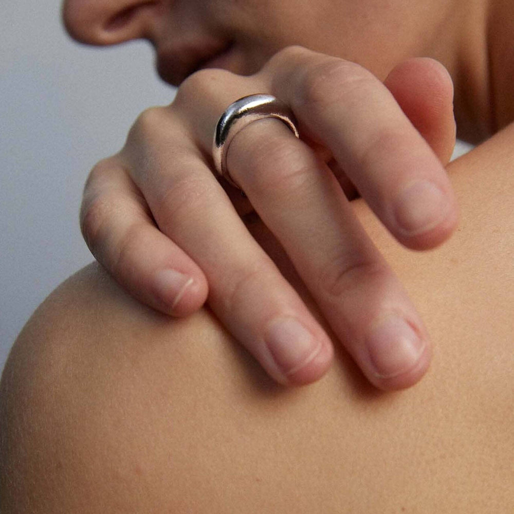 Close-up of a hand with a silver dome ring on a blurred background