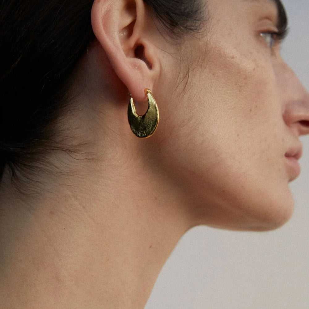 
                  
                    Close-up of a person wearing an oval hoop earring against a neutral background
                  
                