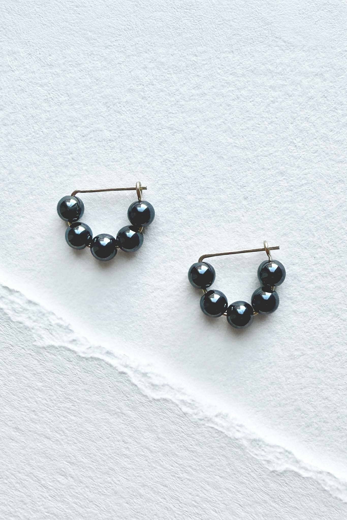 Pair of hematite beaded hoop earrings on a white textured surface