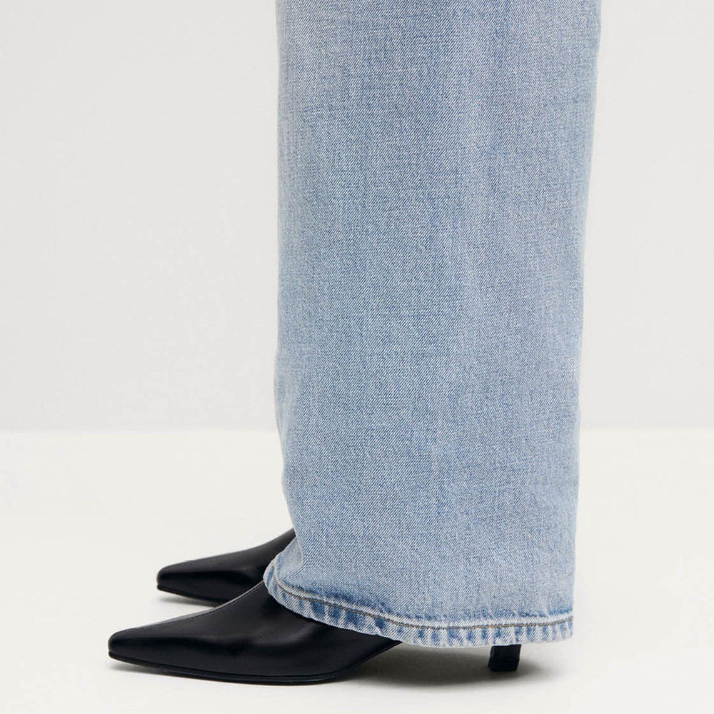 Light blue jeans worn with black heeled boots on a white background