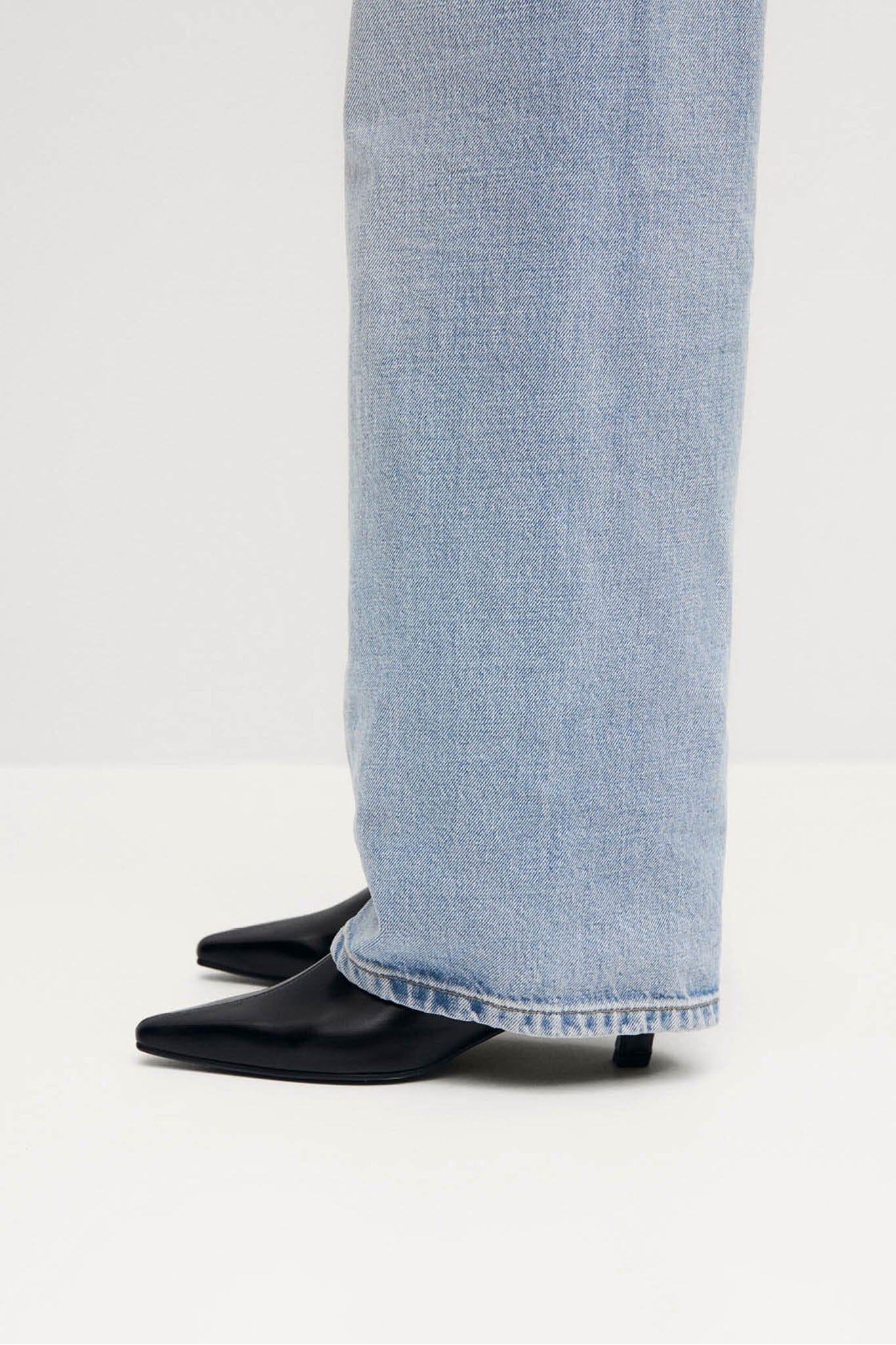 Light blue jeans worn with black heeled boots on a white background