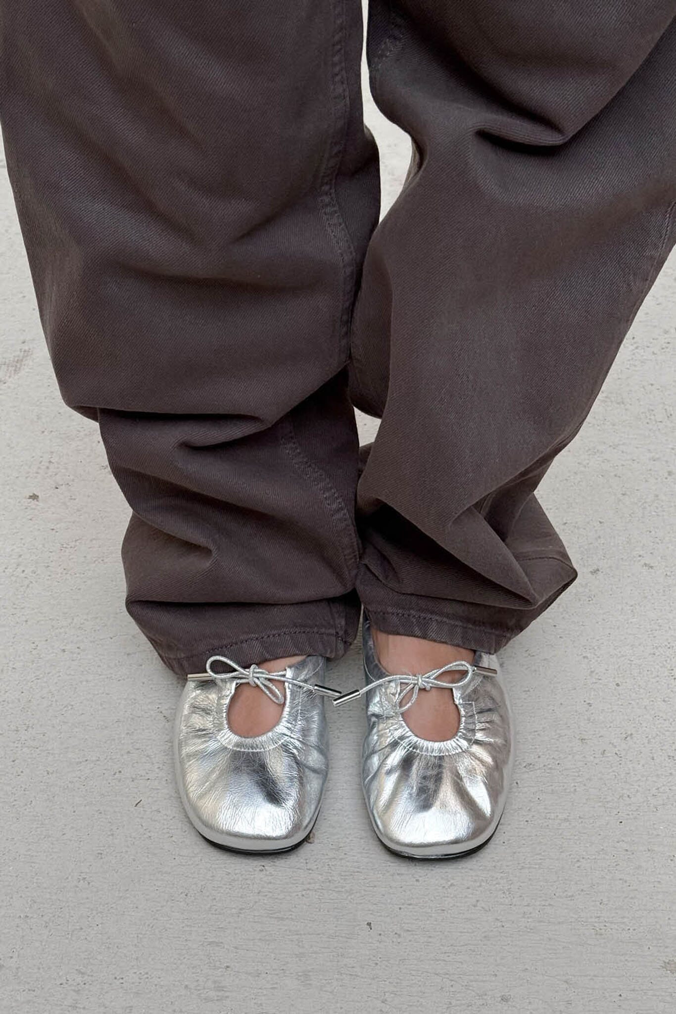 Person wearing silver shoes and brown pants on a plain background