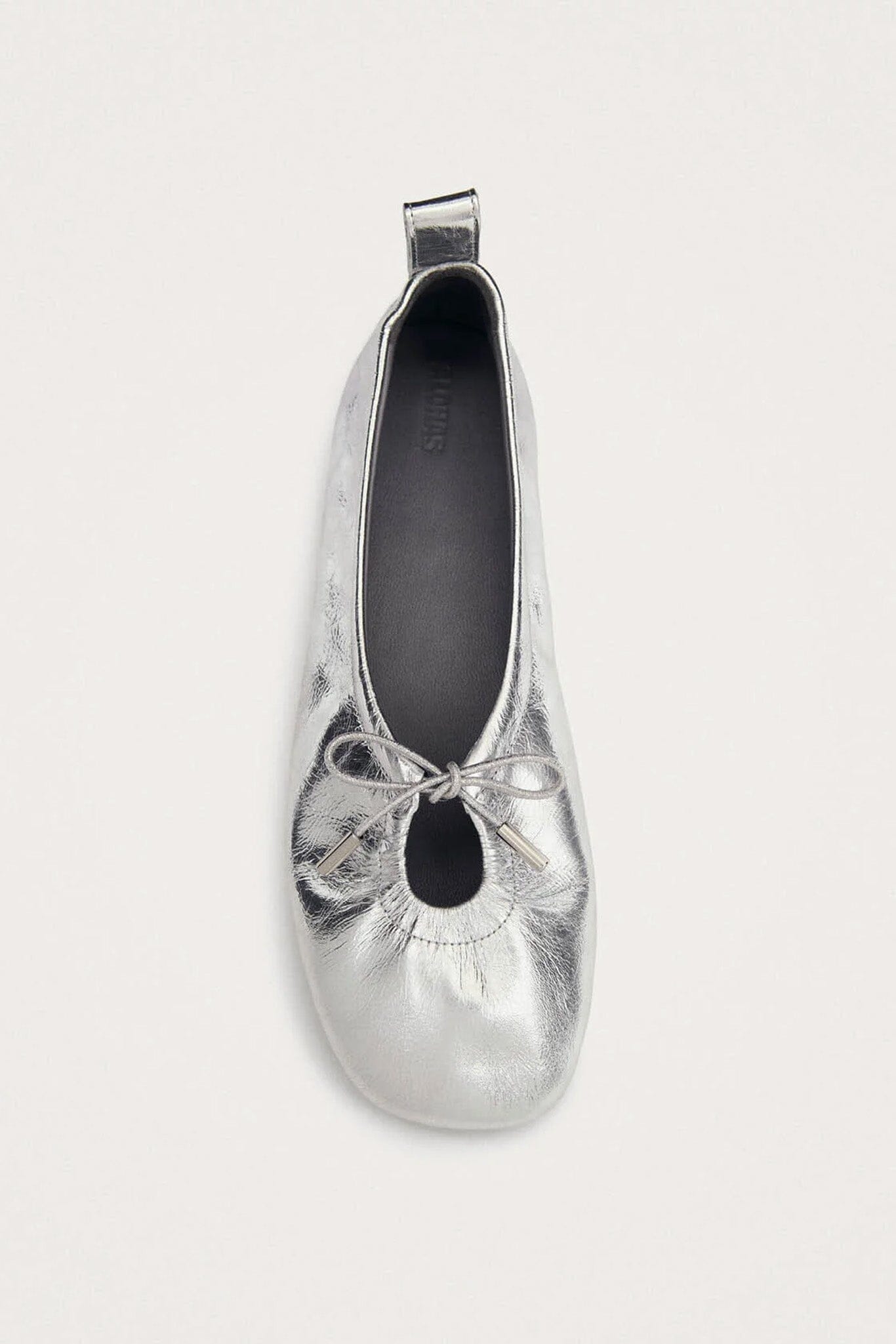 Silver metallic ballerina shoe with a top tie on a white background