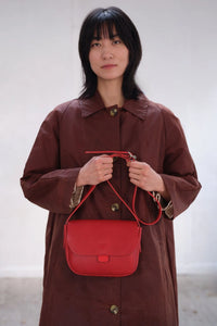 Model holding the London-designed Kate Sheridan Red Orbed Tab Bag. A bold red leather handbag for everyday styling.
