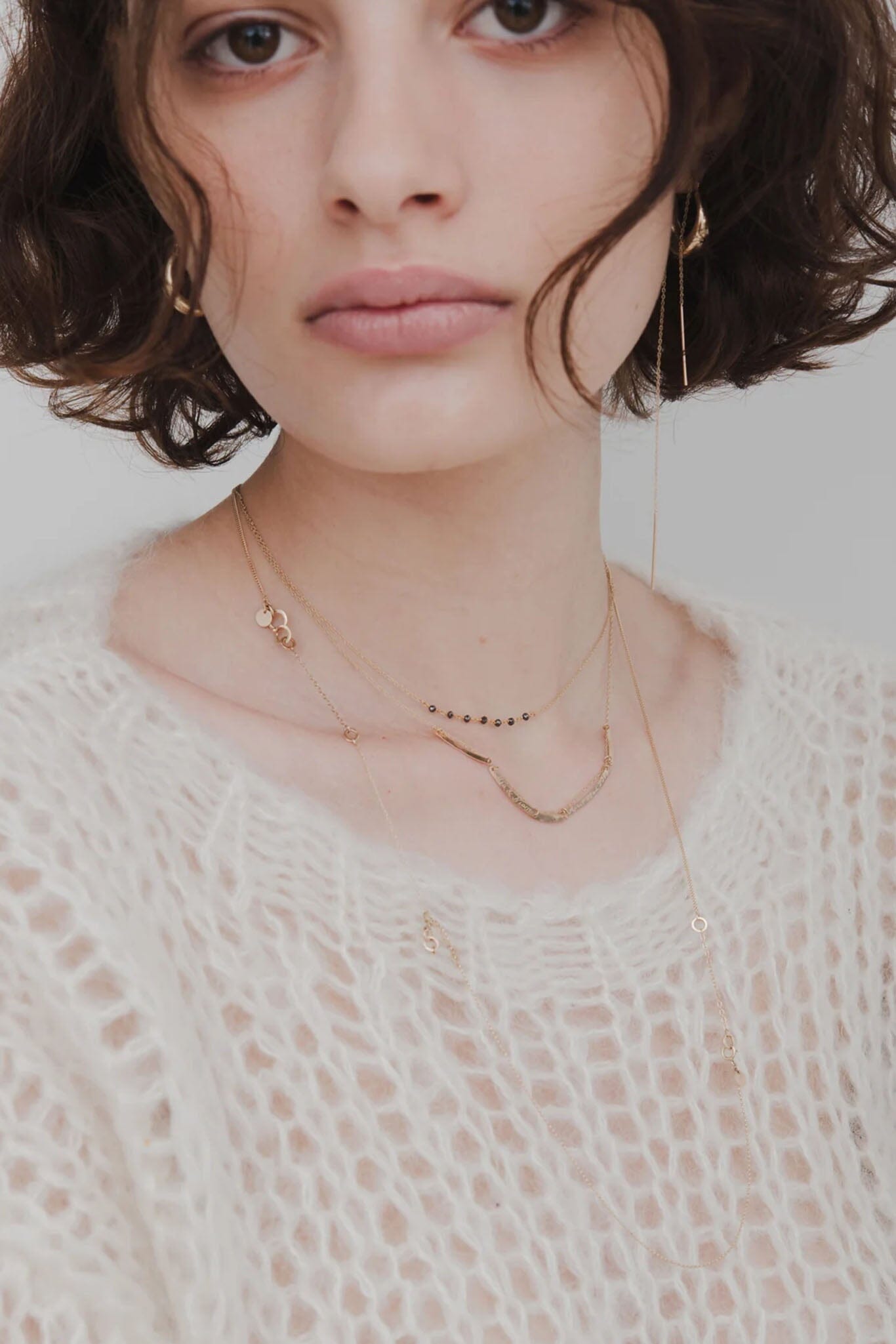 Close-up of a person wearing gold necklaces and earrings against a neutral background