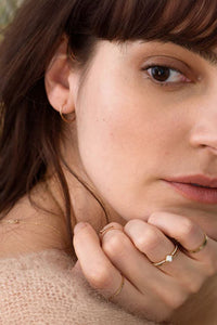 Close-up of a woman's face with a soft focus on her hand and jewelry.