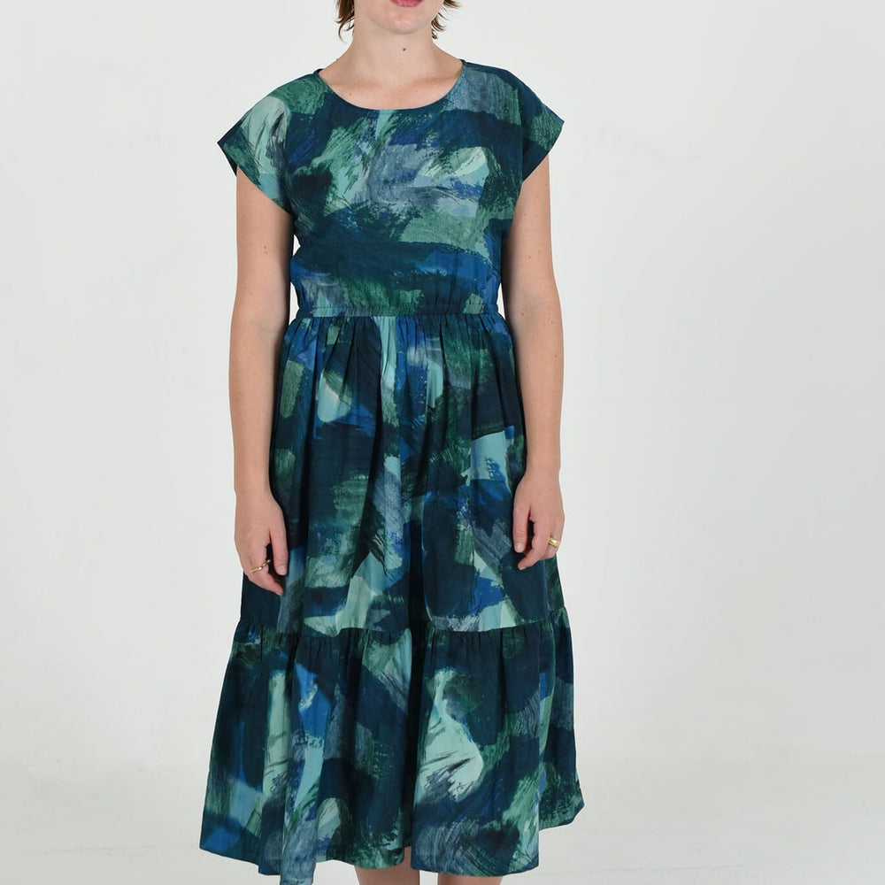 The large M.PATMOS Penelope Dress in Blue Abstract, features a button-down front, midi-length silhouette, waist belt for shaping, and an eye-catching abstract print in blue tones.