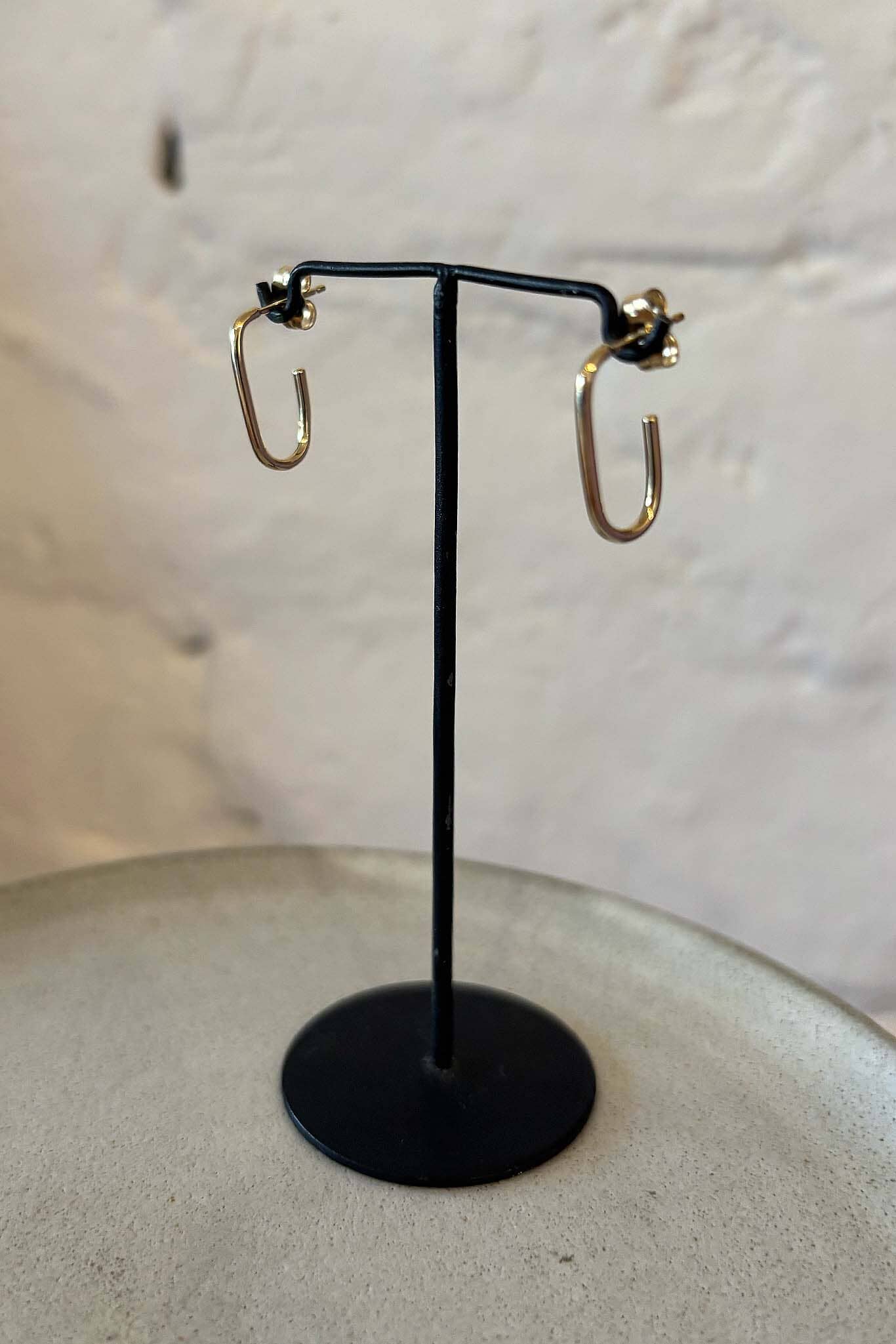 Gold hoop earrings on a black stand against a light background