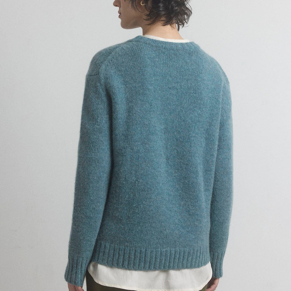 Woman facing the back wearing a blue merino knitted sweater with a plain background