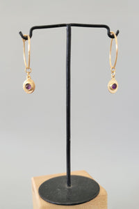 Gold earrings with amethyst gemstones on a black stand against a gray background