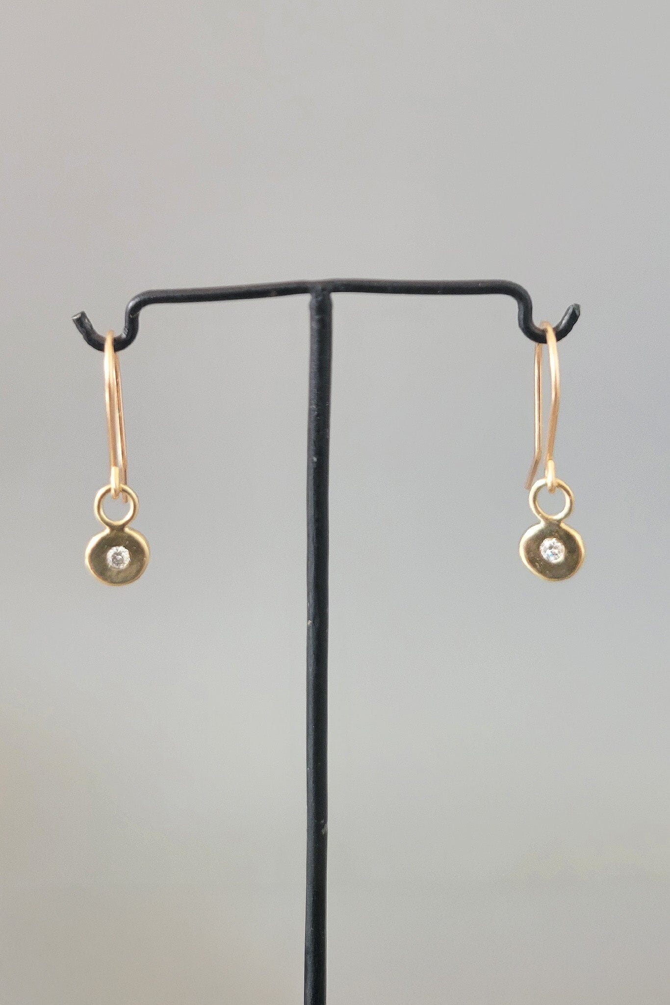 Gold earrings with small round diamonds on a black stand against a gray background