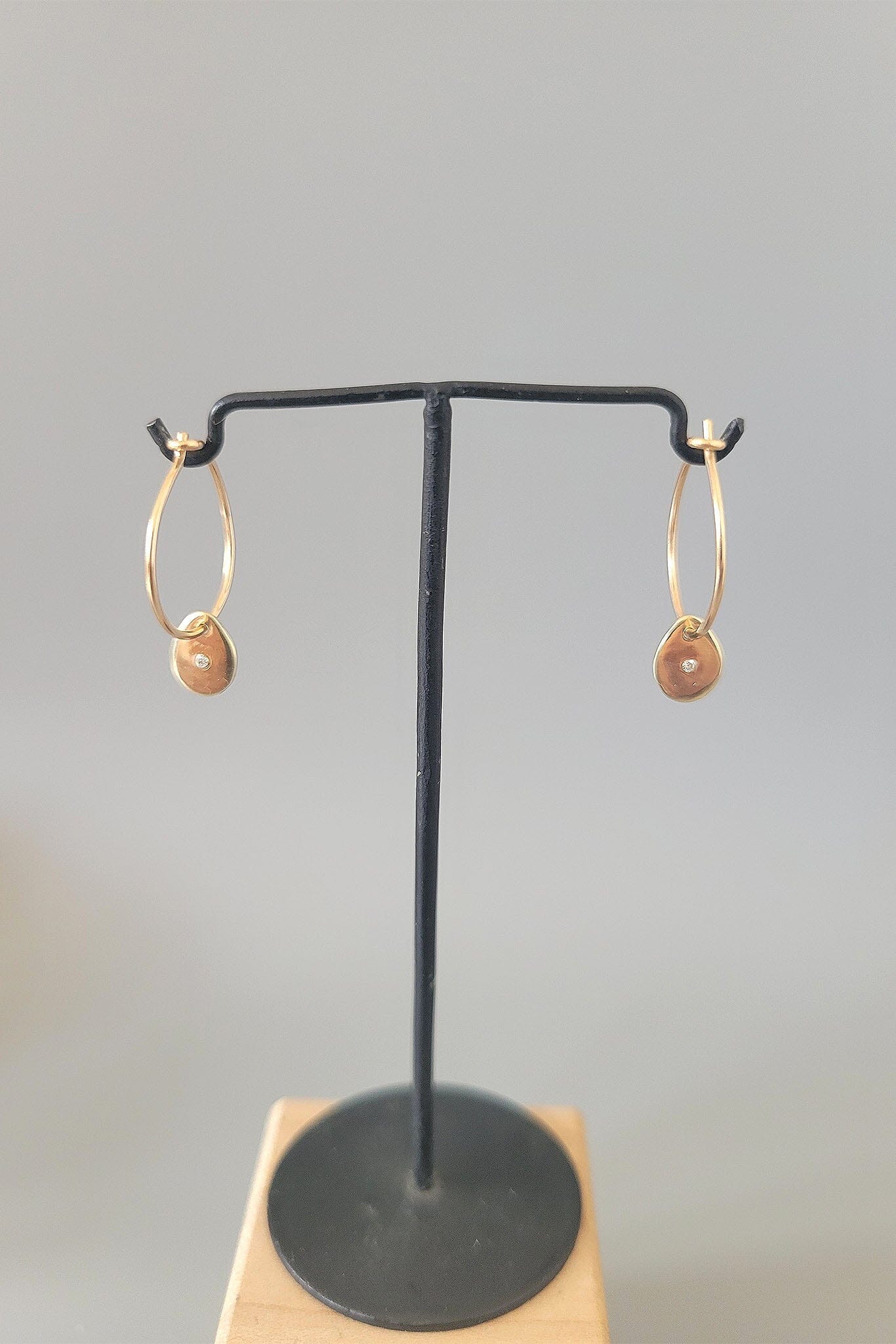 Gold hoop earrings on a black earring stand with a gray background