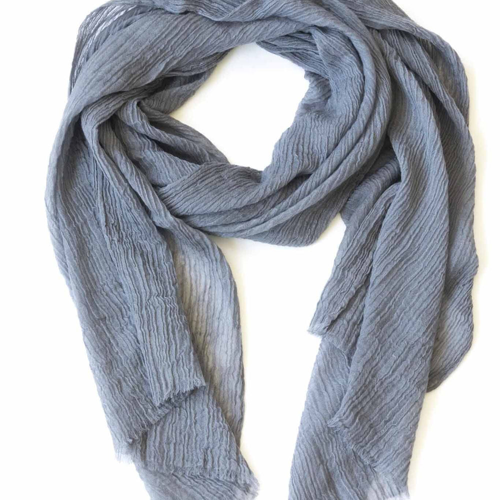 A silver cashmere scarf with pleated design laid out on a plain surface.