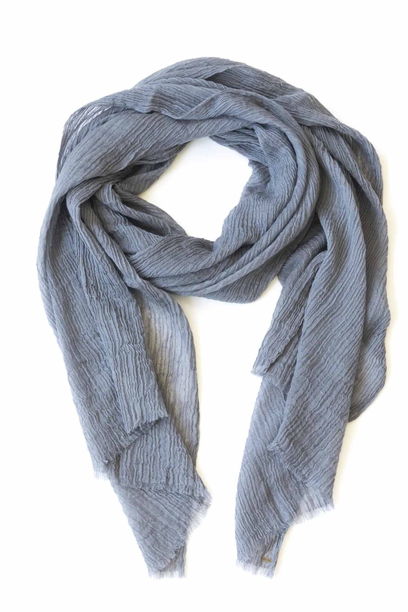 A silver cashmere scarf with pleated design laid out on a plain surface.