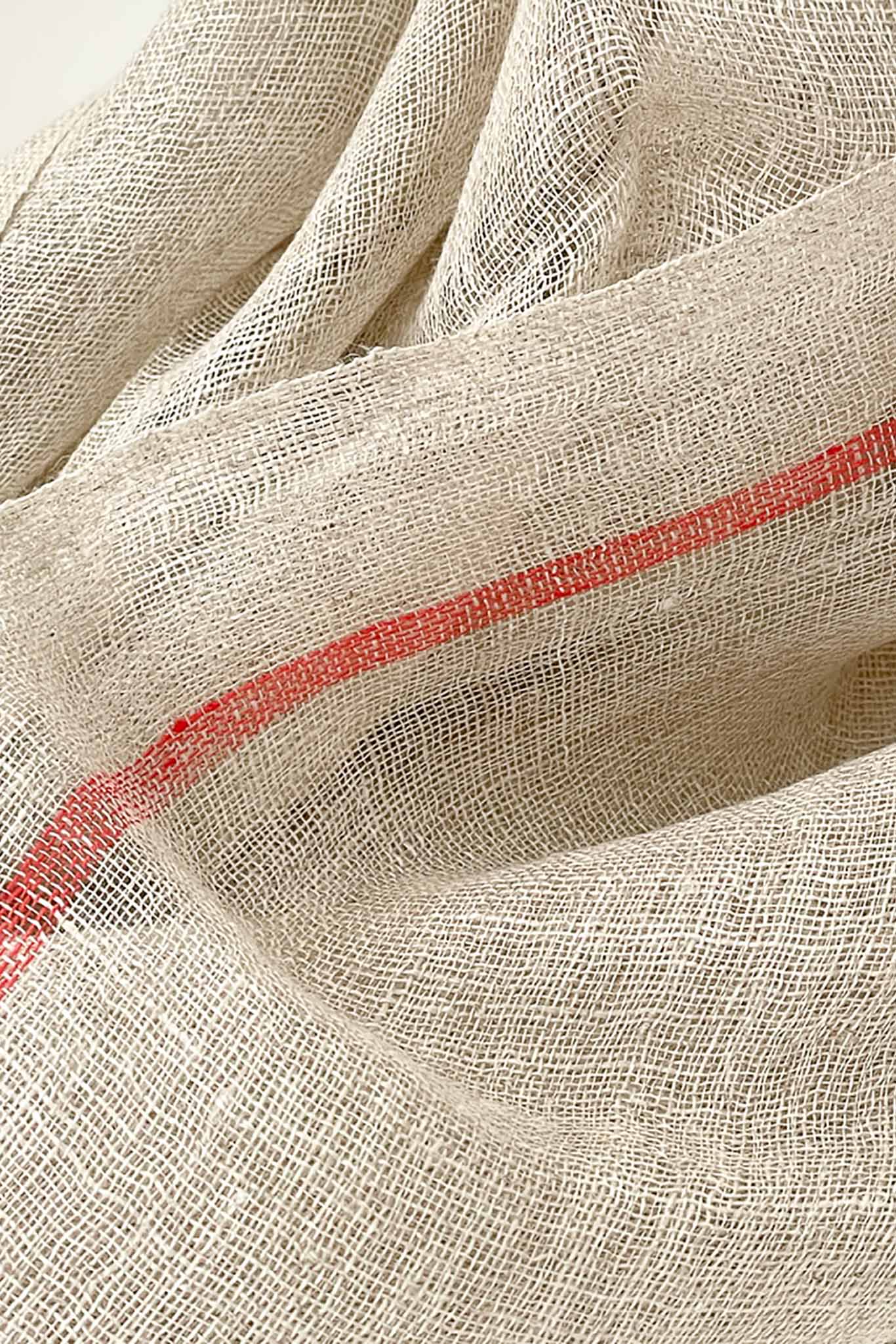 A detailed shot of a handwoven scarf in oatmeal color with orange stripes