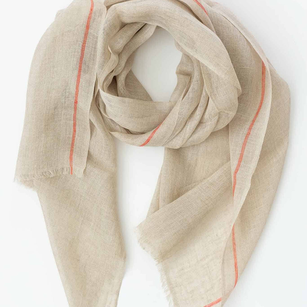 A handwoven scarf in oatmeal color with orange stripes, laid out on a plain surface.