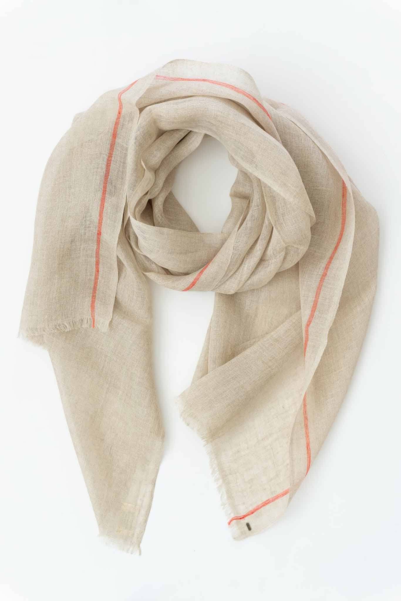 A handwoven scarf in oatmeal color with orange stripes, laid out on a plain surface.