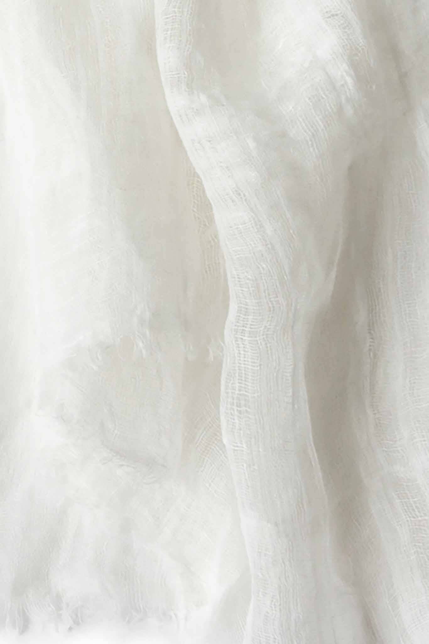 A close up shot of a handwoven, airy white scarf made of linen