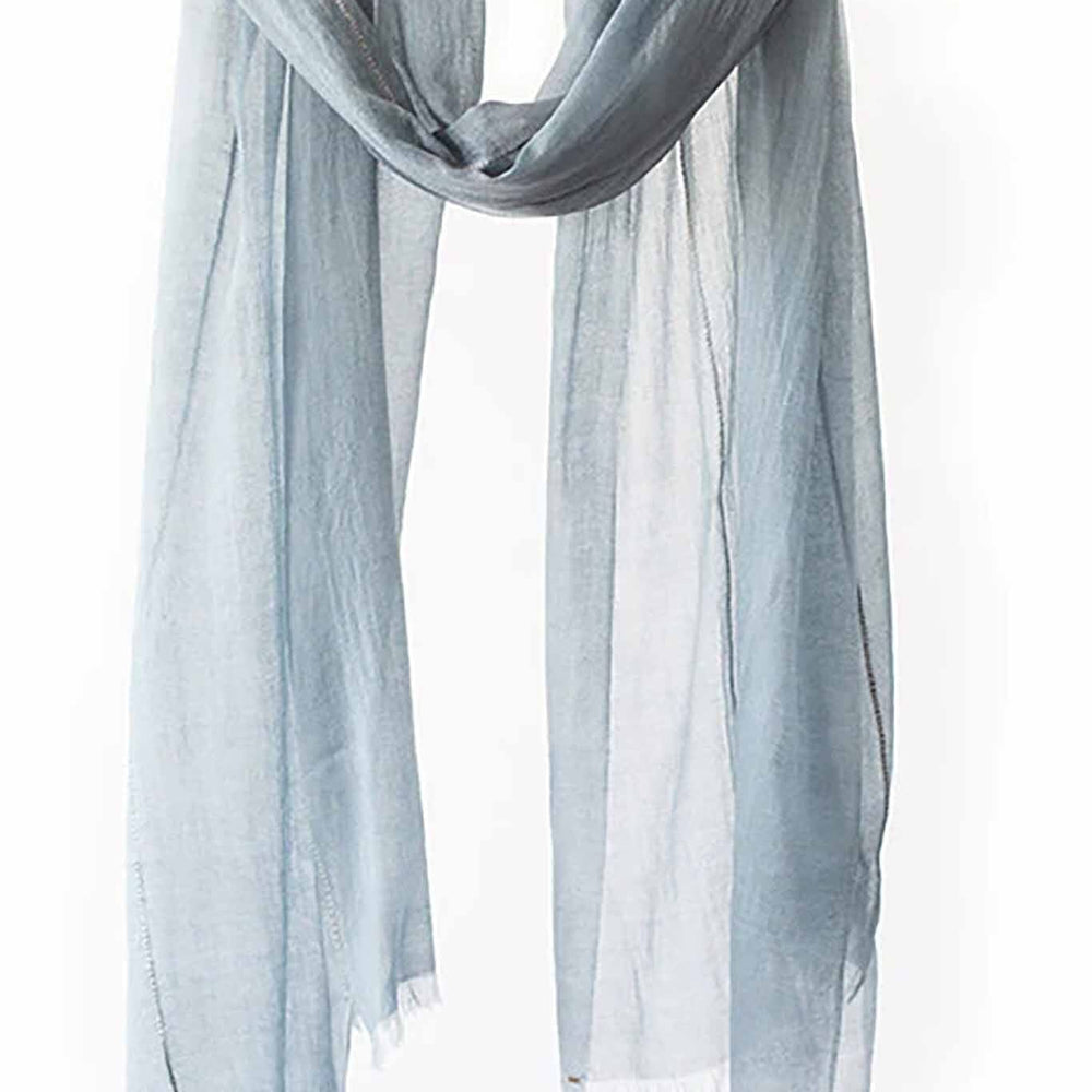 A light blue, sheer scarf with frayed edges displayed on a horizontal rod
