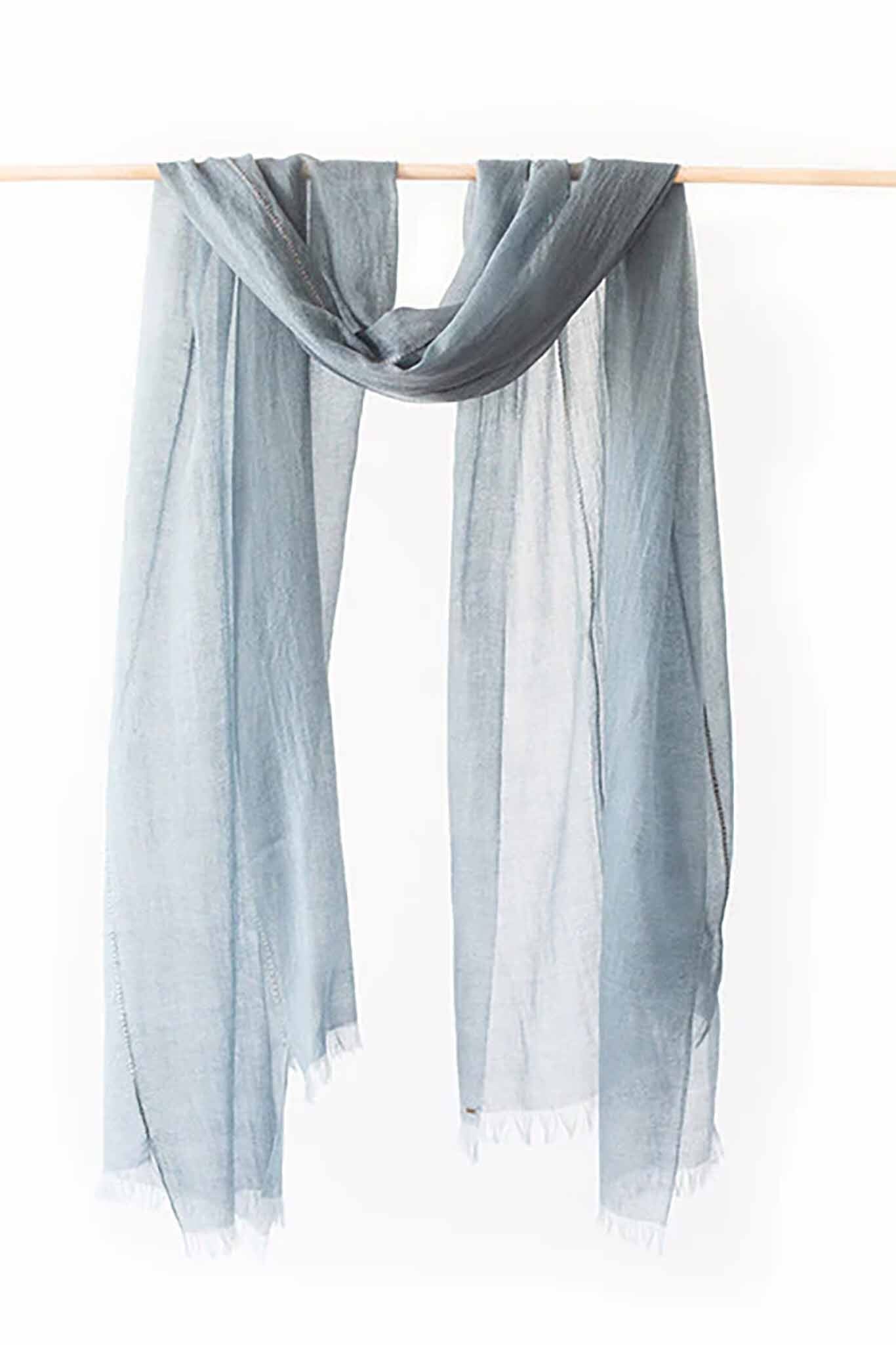 A light blue, sheer scarf with frayed edges displayed on a horizontal rod