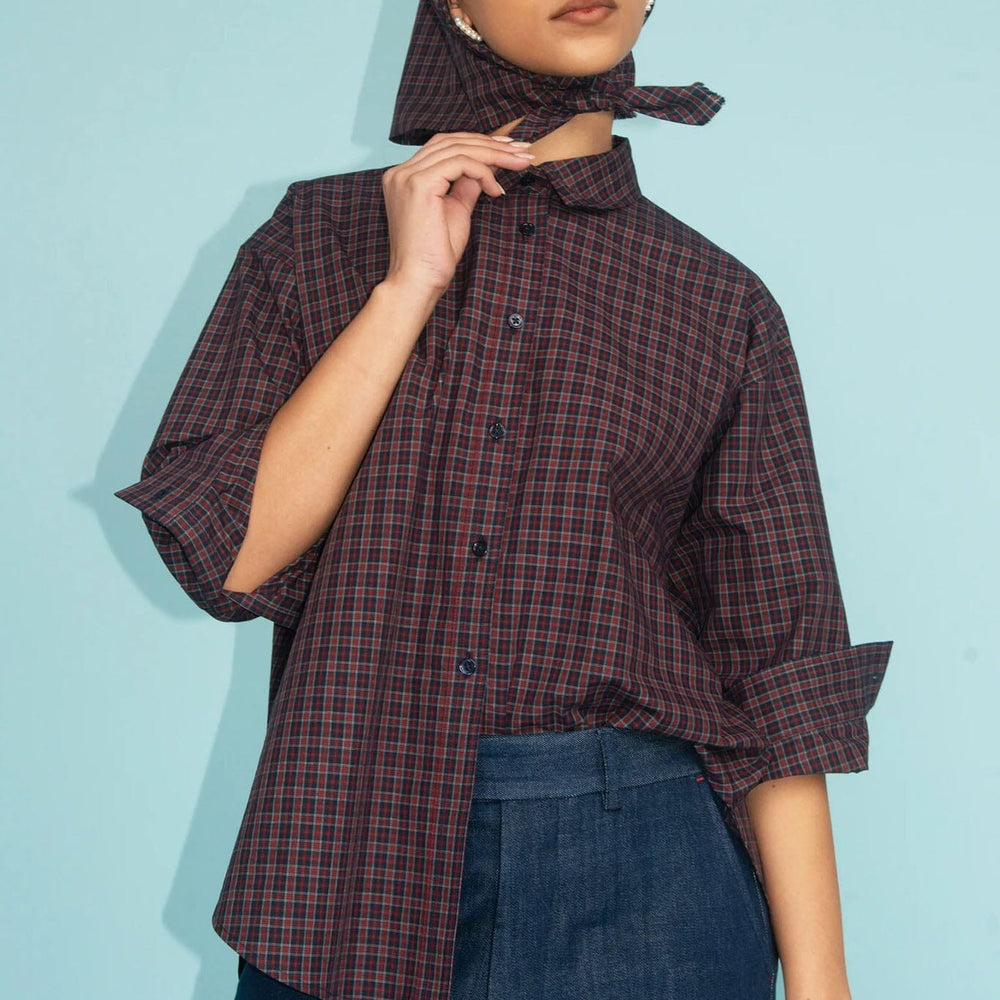 Woman wearing a plaid shirt and scarf against a light blue background