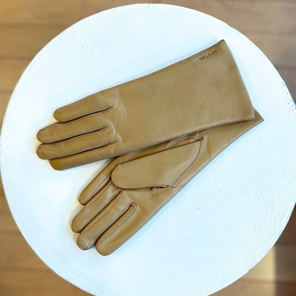 
                  
                    Pair of tan leather gloves on a white circular platform with a wooden background
                  
                