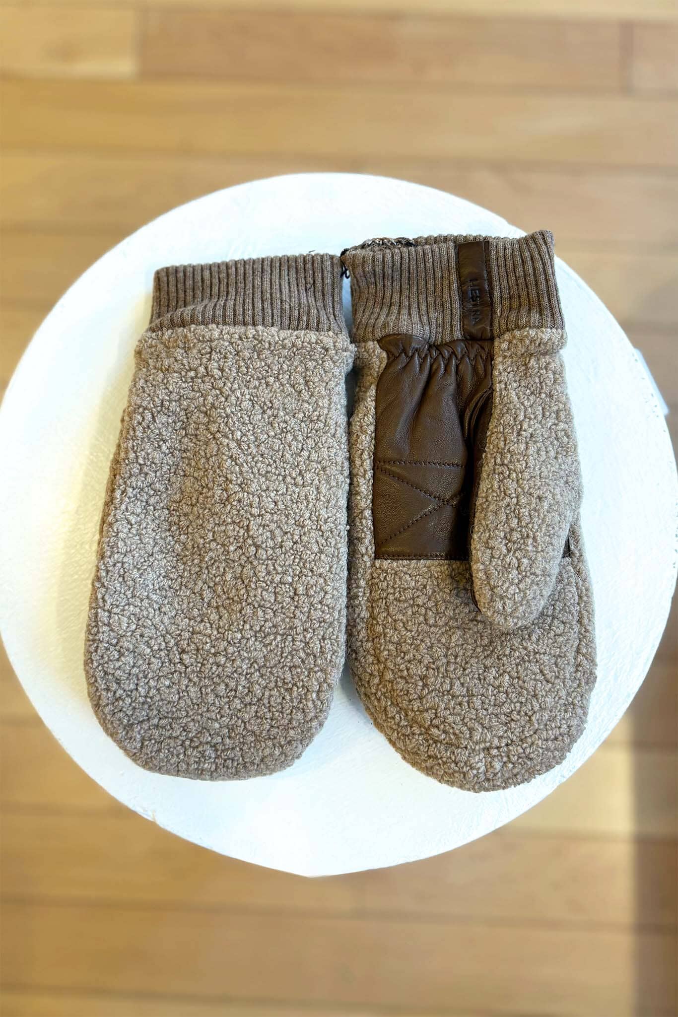 Pair of brown fleece mittens on a white plate with a wooden background