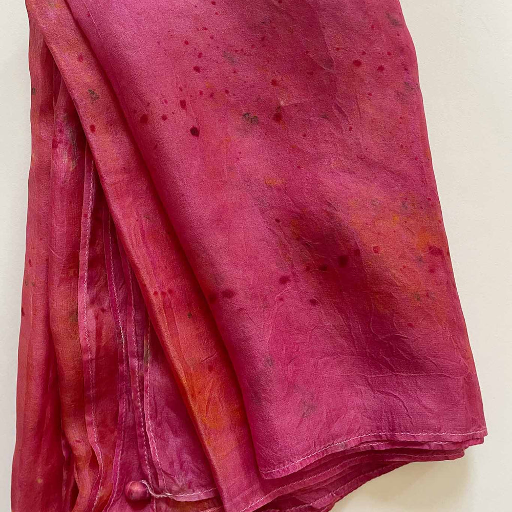 A handcrafted silk scarf with a mix of red and orange hues and natural dye patterns.