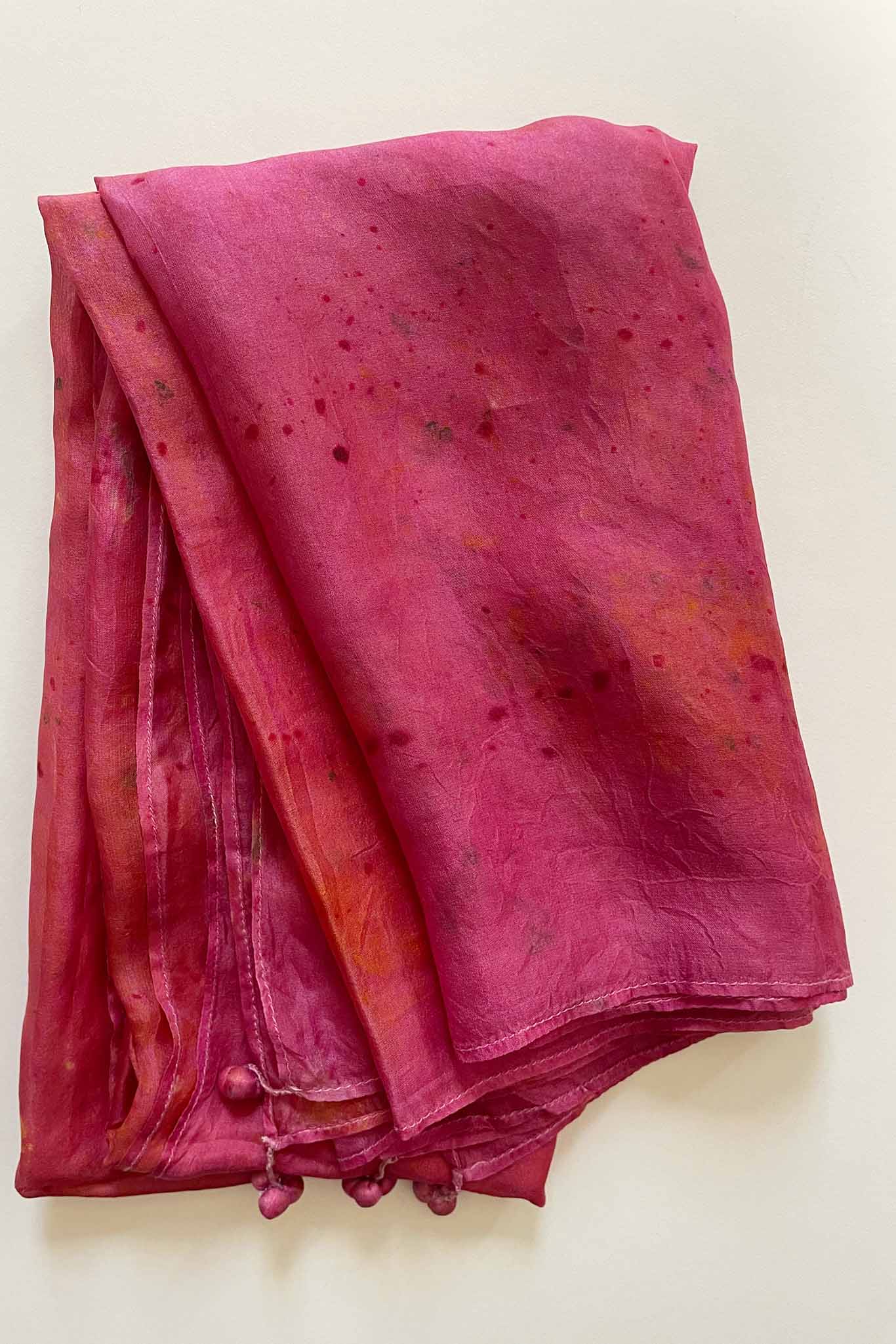 A handcrafted silk scarf with a mix of red and orange hues and natural dye patterns.