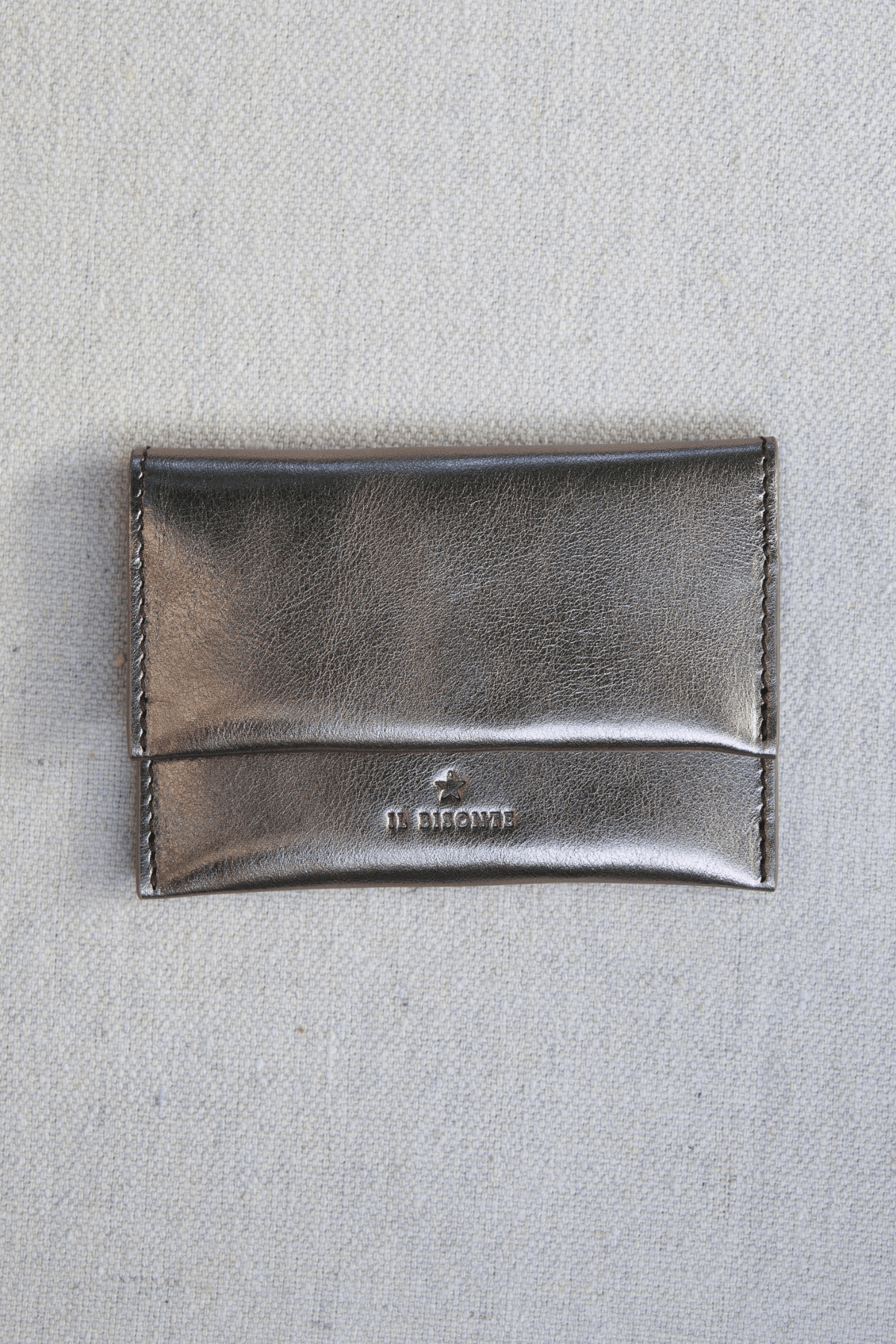 A metallic silver leather card holder with a debossed logo reading 'IL BISONTE' on a textured light gray fabric background.