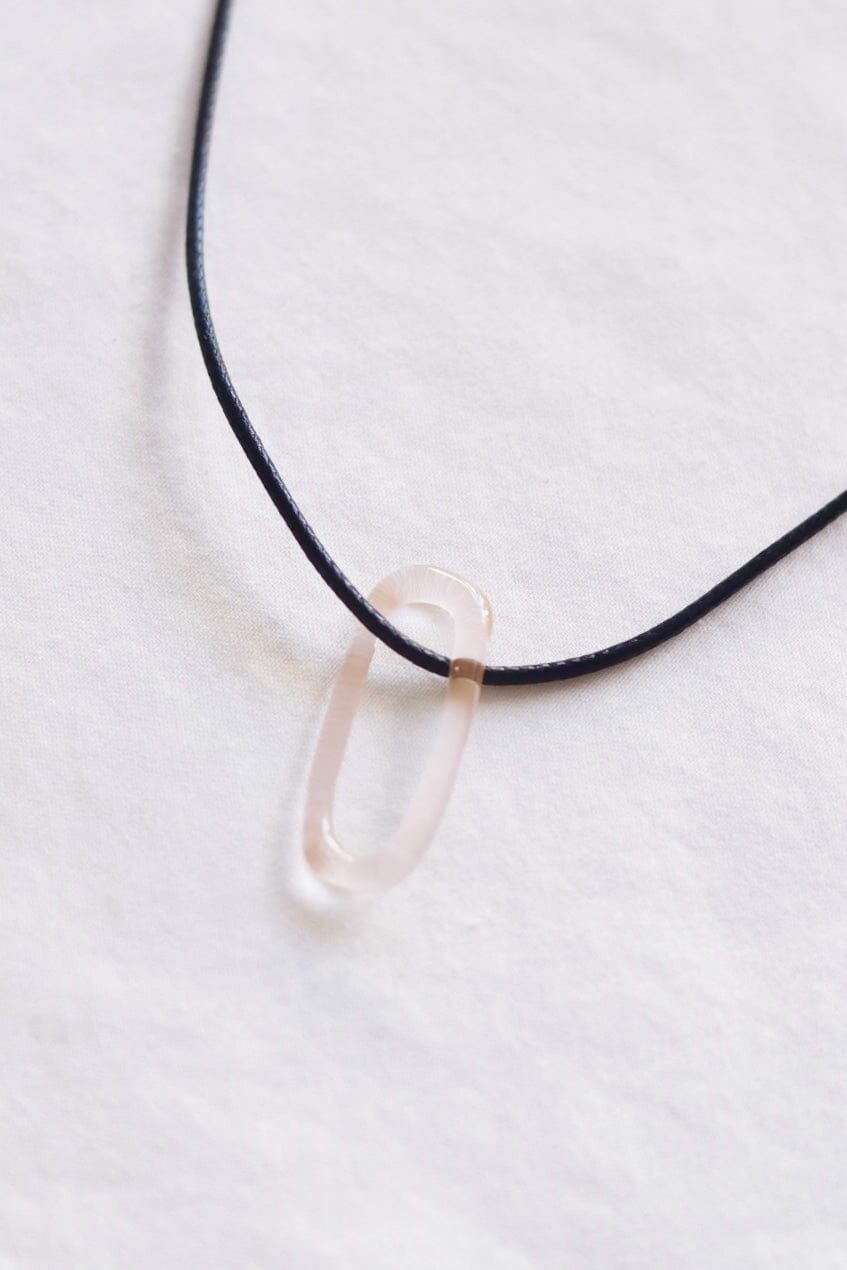 A close up of a pink oval glass pendent on a black cord necklace