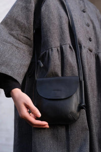 Model holding the London-designed Kate Sheridan Black Mini Ribbon Bag. A compact black leather crossbody for everyday wear.