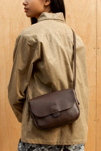Model wearing the London-designed Kate Sheridan Chocolate Orbed Tab Bag. A classic brown leather crossbody for everyday.