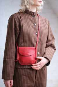 Model wearing the London-designed Kate Sheridan Red Mini Ribbon Bag. A vibrant red leather crossbody purse.