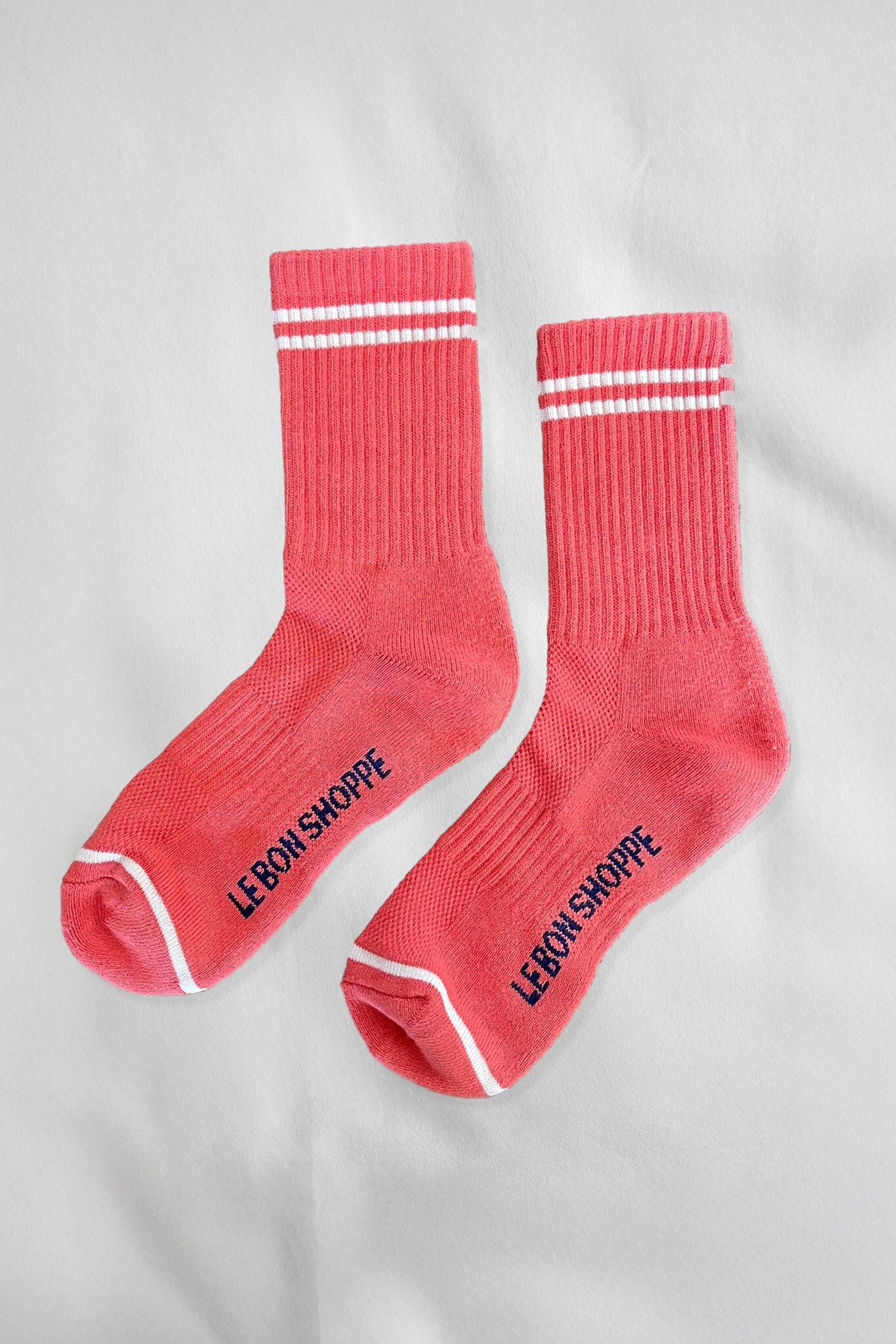 A pair of calf-length coral pink socks with white stripes and the text 'LE BON SHOPPE' on the side.