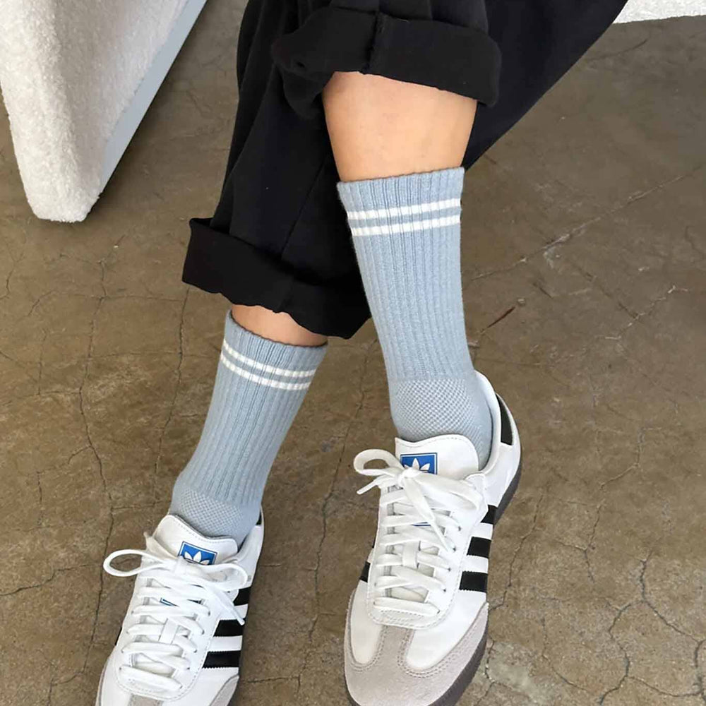 A person wearing calf-length blue grey socks with white sneakers, the socks reach mid-calf and have a striped pattern near the top.